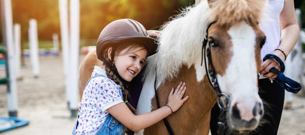 Cute little girl and her older sister enjoying with pony horse outdoors at ranch.